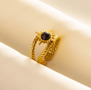 Detail of gold double-layer sun ring with black stone on soft fabric background
