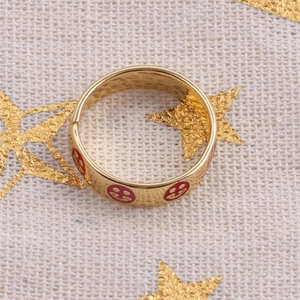 Polished gold ring with red enamel smile face pattern on beige fabric background