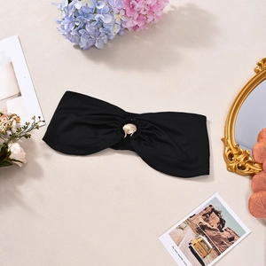 Detail of black strapless bikini top with golden shell buckle on a beach decor background