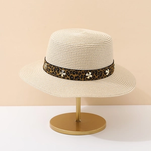 Detail of beige straw hat with leopard print ribbon and silver cross studs on a stand