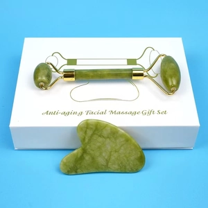 Macro shot of green jade face roller and heart gua sha tool in a white gift set box