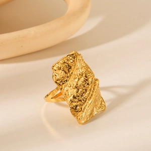 Detail view of gold geometric ring with hammered texture on a cream background