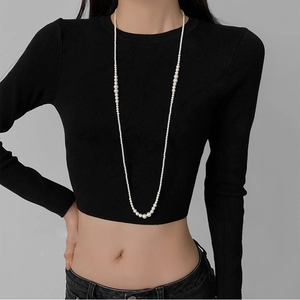 Close-up of model wearing minimalist long pearl necklace with gradient sizes on black top