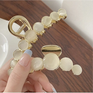 Macro detail of large gold metal hair claw clip with elegant white cat eye stone beads