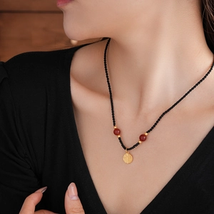 Detail of red bead necklace with gold Fu character pendant on a black woven cord