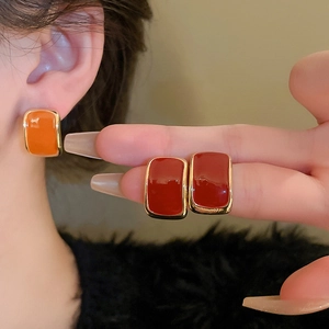 Close-up of vintage square enamel earrings in orange and dark red with gold trim