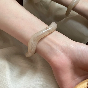 Detail of cream wavy resin bangle with marble texture worn on wrist with mirror reflection