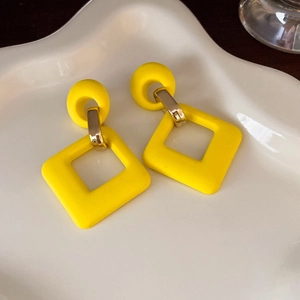 Close-up of yellow geometric acrylic earrings on a white decorative plate with matte finish