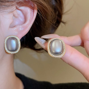 Macro detail of oval gold earrings featuring a grey gemstone and pavé zircon accents