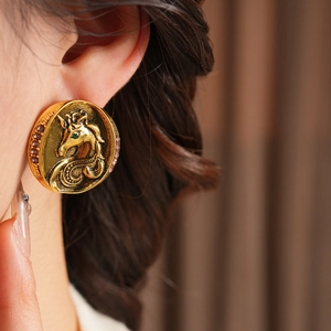 Detailed macro view of vintage gold unicorn earrings with pink crystals and green gemstone eye