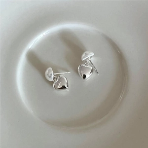 Macro detail of silver heart-shaped pearl earrings on a white porcelain dish