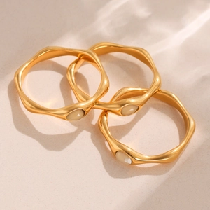 Three-piece gold wavy rings set with oval pink crystals on natural beige sand background