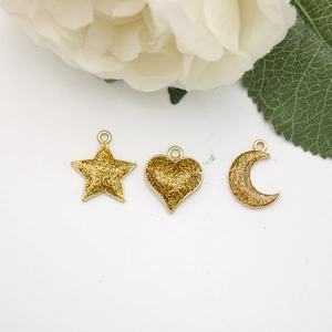 Close-up of heart, star, and moon gold charms with glitter enamel and a white rose