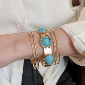 Detail of gold layered bracelets featuring turquoise stones and smooth metallic finish