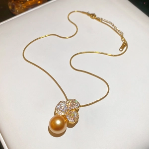 Detailed macro of gold-plated clover pendant with zircon crystals and large golden pearl