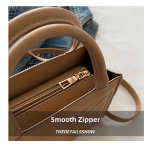 Detail shot of the smooth gold metal zipper closure on the beige quilted crossbody bag