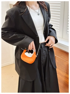 Close-up of mini orange bag with metal top handle and silver chain strap on model