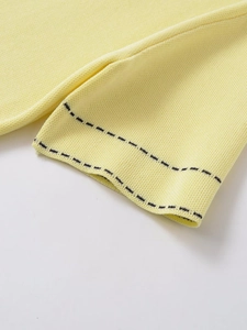 Detail of light yellow polo cardigan showing fine knit texture and black dotted stitching
