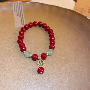 Vue détaillée du bracelet en perles de cinabre rouge avec breloque Fu dorée