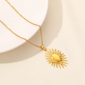 Close-up of golden sunburst eye pendant on stainless steel chain over a ceramic plate