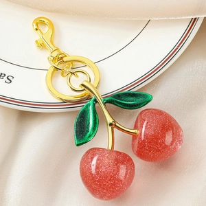 Close-up of glittery red resin cherry keychain with golden lobster clasp and green leaves