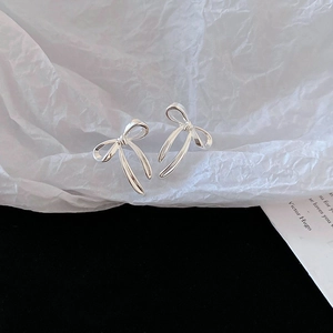 Gros plan sur des boucles d'oreilles nœud en argent et perles sur un fond blanc texturé