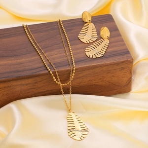 Golden stainless steel hollow leaf jewelry set with zircon on dark wood and yellow satin