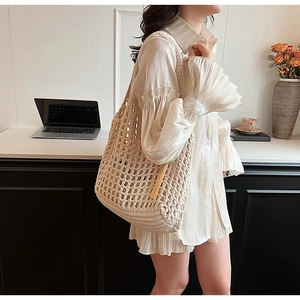 Close-up of beige woven tote bag featuring hollow mesh knit design and tassel detail