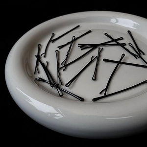 Minimalist black metal hair pins in white ceramic dish against a black background