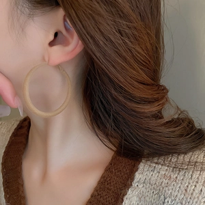 Close-up of model wearing large matte light brown flocked geometric hoop earrings