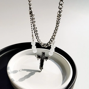 Detail of layered silver Cuban chain with black lava cross pendant and white beads