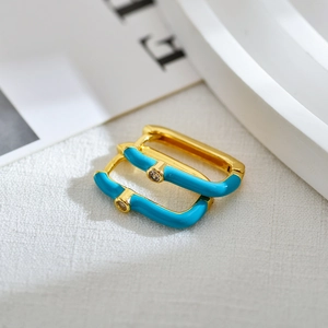 Vue macro de boucles d'oreilles dorées rectangulaires avec émail bleu et pierre zircon