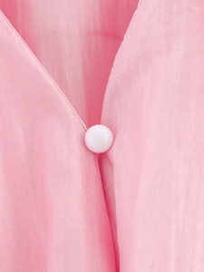 Gros plan détaillé du col en V rose avec bouton blanc et texture de tissu légère