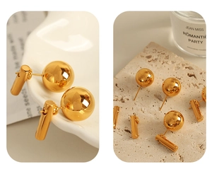 Macro view of gold spherical stud earrings with cylindrical pendants on a textured stone