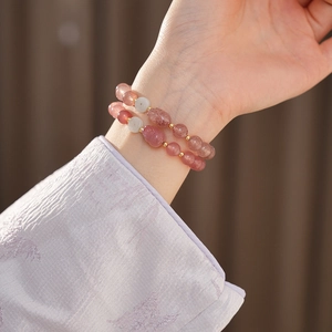 Detail of pink strawberry quartz bracelet with cat charm and gold accents on wrist