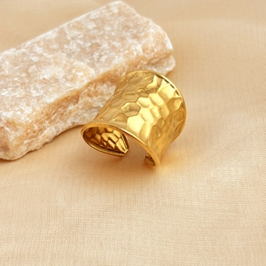 Golden wide open ring with hammered texture on a beige fabric with a natural stone