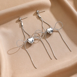 Detailed macro shot of silver bow heart earrings on elegant champagne silk fabric