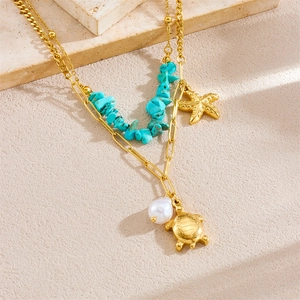 Gold layered necklace with turquoise stones, starfish, pearls and turtle pendants on stone