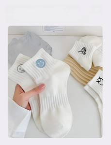 Detail of white ribbed cotton socks featuring cute cartoon embroidery on a wooden tray