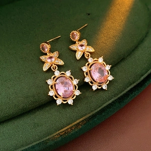 Macro shot of vintage style gold earrings with pink zircon on dark green velvet
