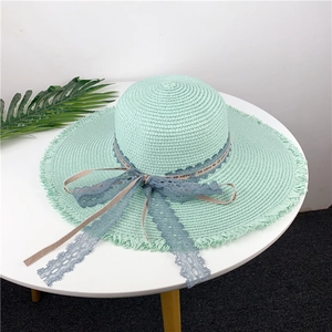 Detail of mint green straw hat featuring frayed edges and blue decorative lace ribbon