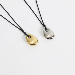 Macro detail of minimalist gold and silver bean pendants on black leather cords