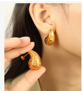 Close-up of golden teardrop stud earrings featuring a hammered metal texture on a model