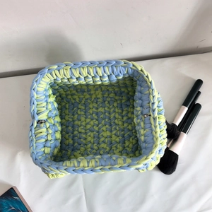 Detailed top view of a handmade blue and lime green crochet basket with makeup brushes