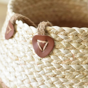 Detail of woven straw basket featuring natural textures and brown leather handles