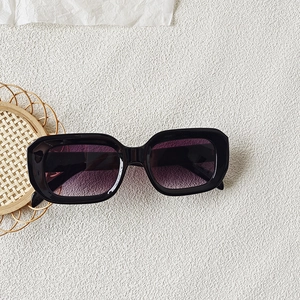 Detail shot of black square sunglasses with gradient purple lenses on a white textured background