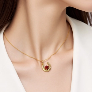 Detail of a U-shaped gold necklace with a red gemstone and white crystals on a model