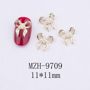 Détail de breloques nœud doré 11x11mm avec perles sur manucure rouge vive