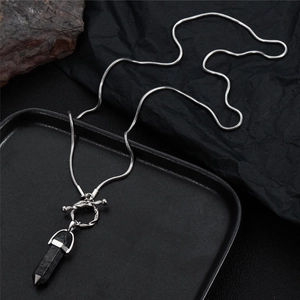 Detail of silver snake chain with black hexagonal pillar pendant on dark stone