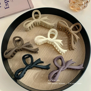 Overhead view of six matte bow-shaped acrylic hair claws in assorted neutral colors